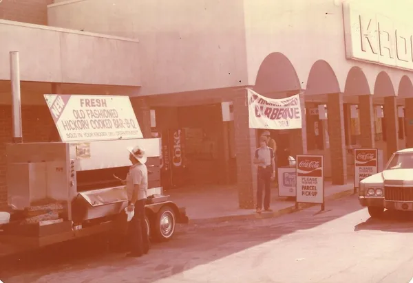 A mobile smoker set up outside a grocery store under a barbecue banner