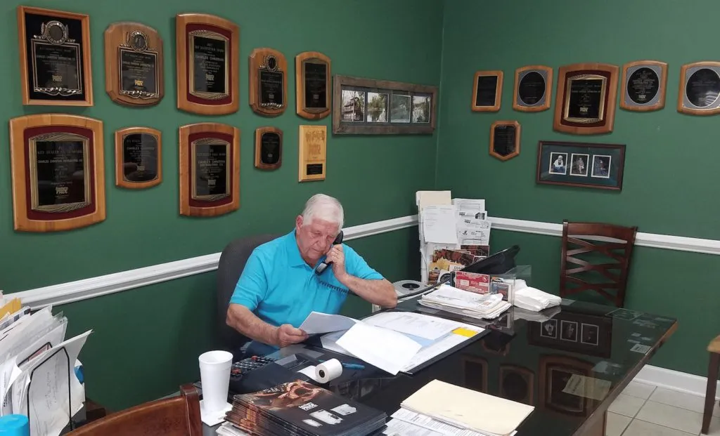 At the office desk, with framed awards on the wall behind